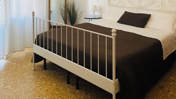 A bedroom with a bed, a chandelier, a mirror, and a wall art piece. - Novella Italy (Florence)