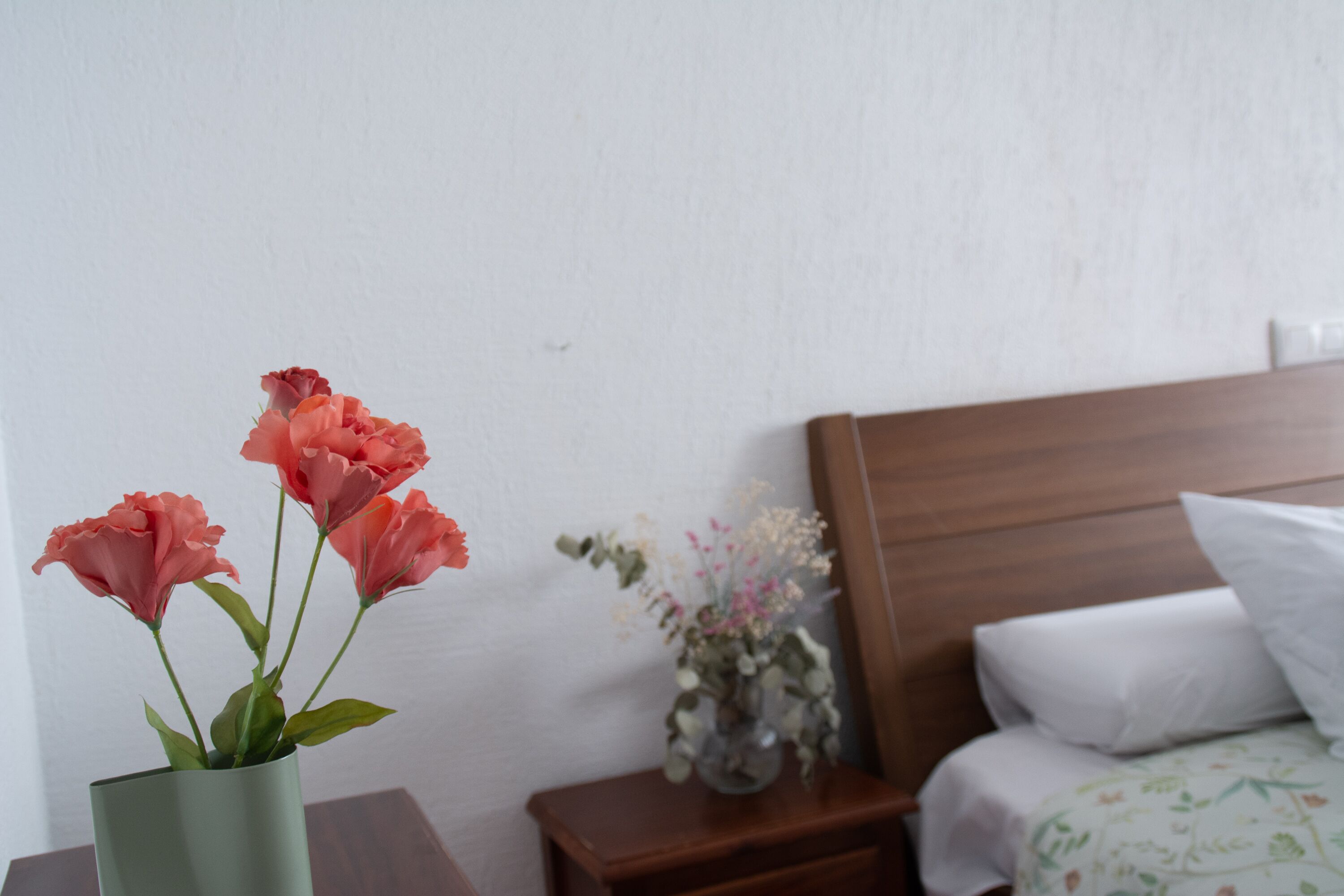 Un dormitorio con cabecera de madera, una mesita de noche con un florero y una cama con ropa de cama blanca.