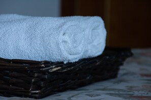 A white towel rolled up and placed on a dark wicker basket.