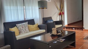 Uma sala de estar com sofá, duas poltronas, uma mesa de centro e uma luminária.