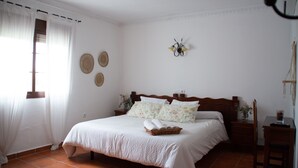 Quarto com uma cama grande, mesa de cabeceira, uma cadeira e escrivaninha.