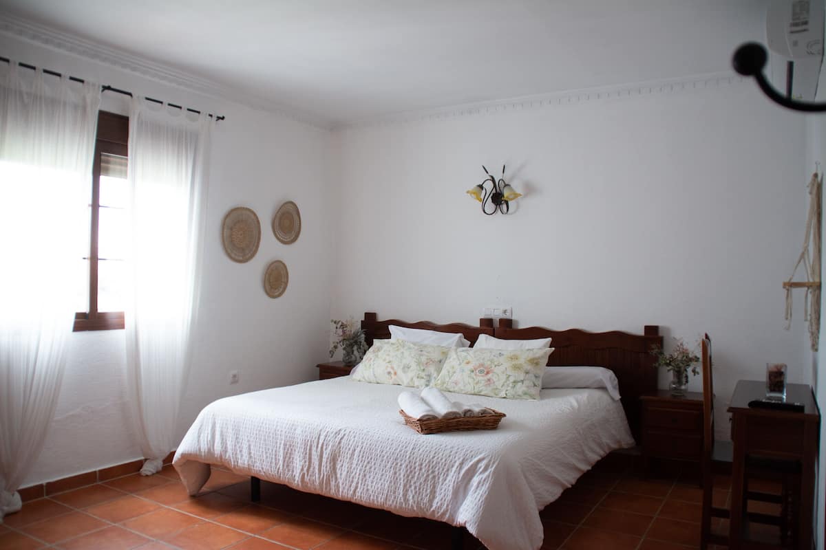A bedroom with a large bed, a nightstand, a chair, and a desk.