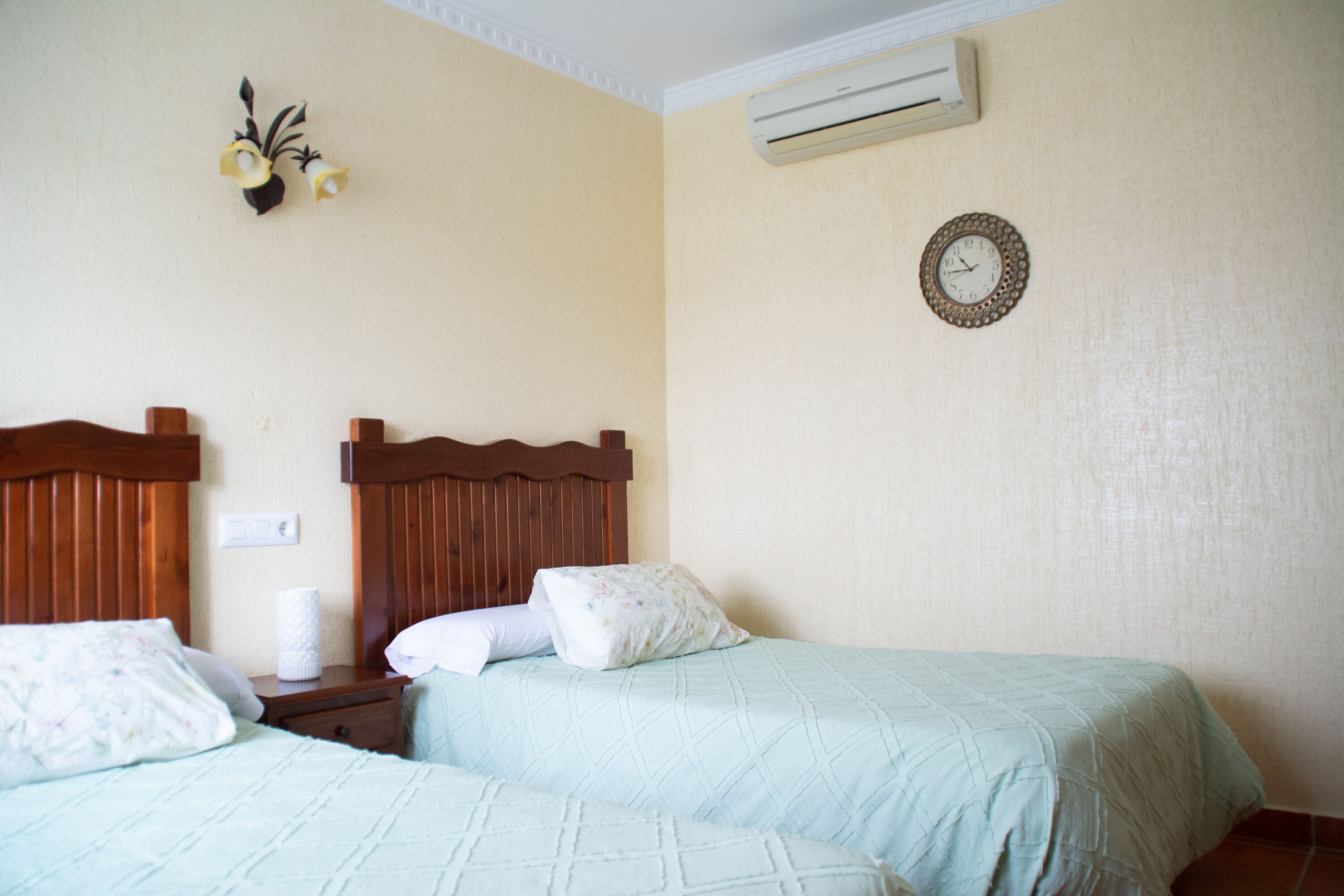 Una habitación de hotel con dos camas, cabeceros de madera, un reloj de pared y un equipo de aire acondicionado.