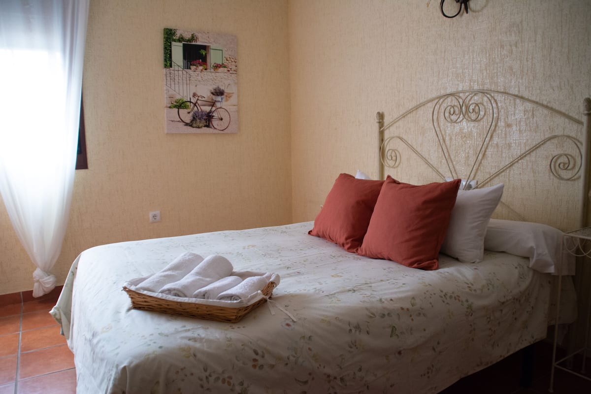 A neatly made bed with a floral bedspread, two pillows, and a basket of folded towels.