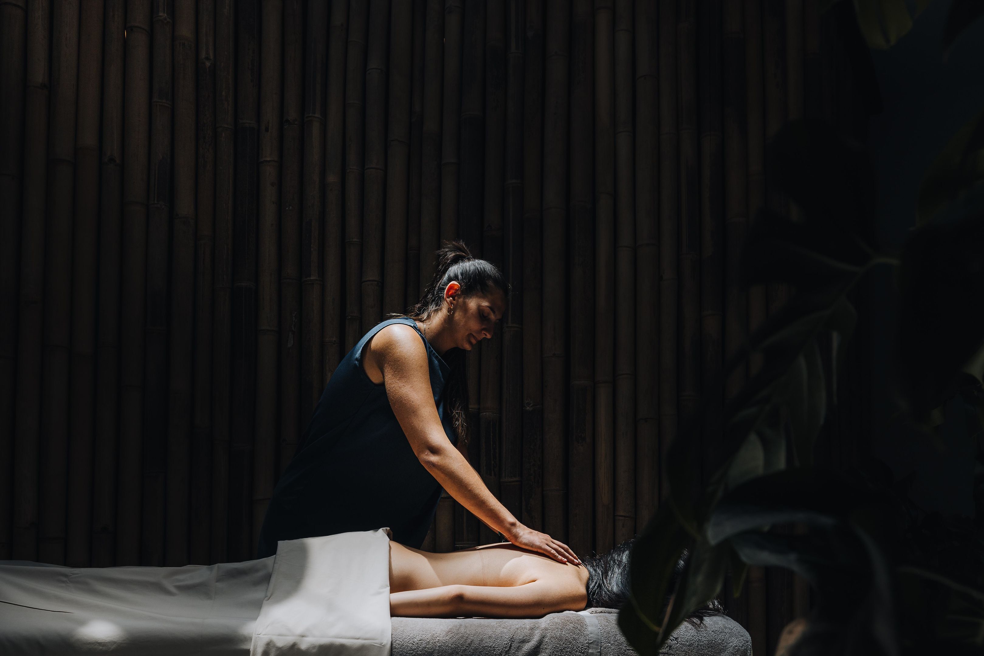 A person receiving a massage in a room with a bamboo wall.