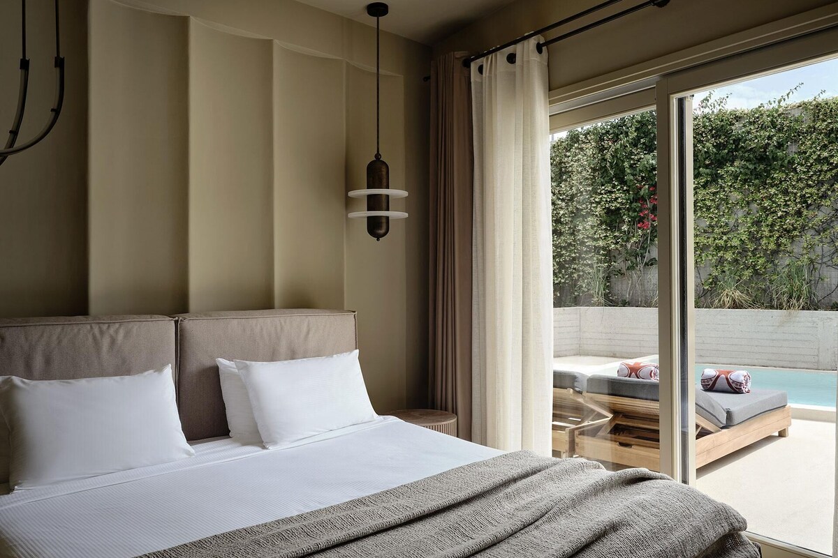 Een moderne hotelkamer met een groot bed, een hanglamp en uitzicht op een buitenzwembad.