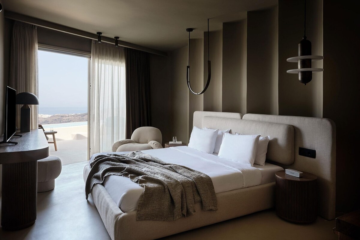 Een moderne hotelkamer met een groot bed, een bureau en uitzicht op zee.