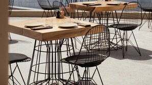 A seaside restaurant with outdoor seating, tables, and chairs, overlooking the ocean and rocky cliffs.
