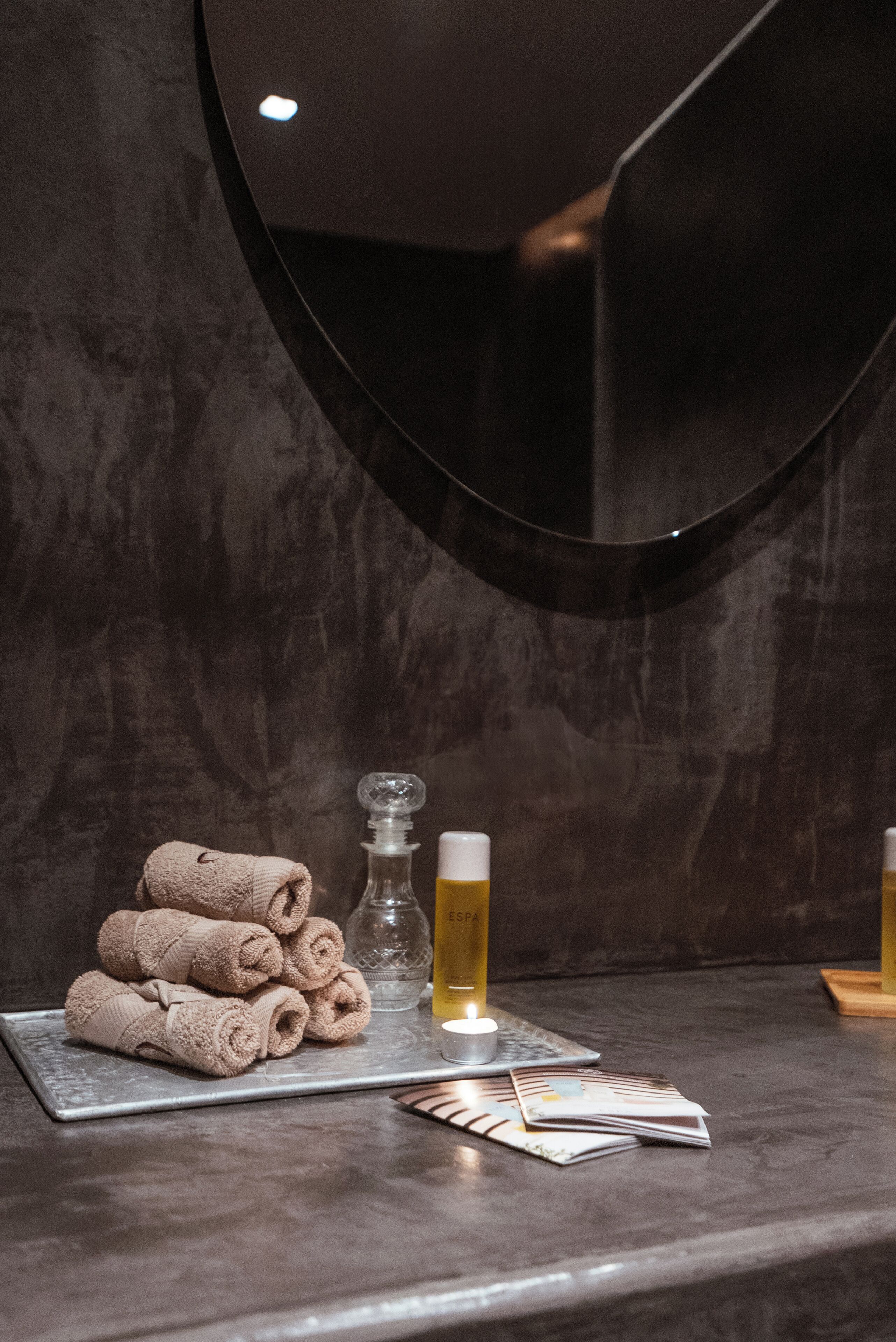 A spa area with towels, a candle, and a glass of beer on a marble countertop.
