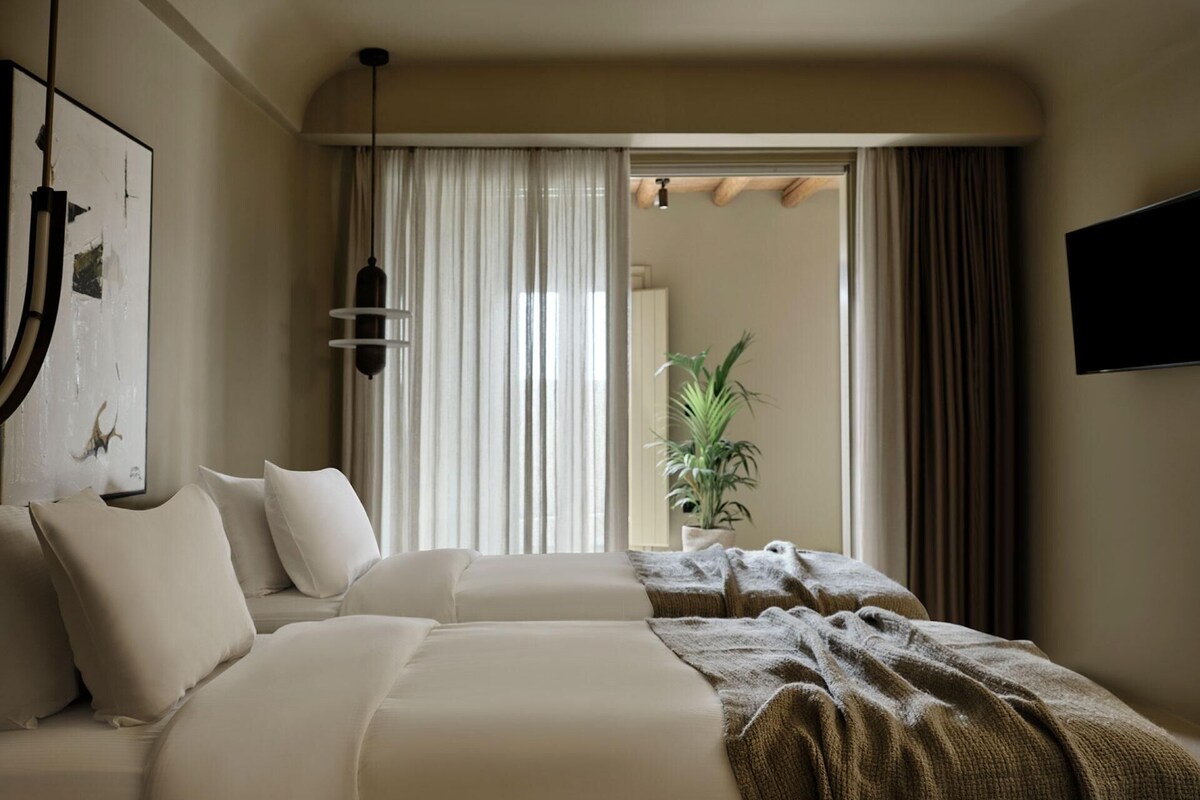 Een hotelkamer met een groot bed, een plant in een pot en een televisie aan de muur.