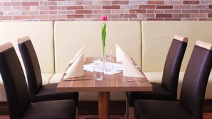 A dining table with four chairs, a vase with a single flower, and a brick wall in the background. - Baums Rheinhotel (Boppard)
