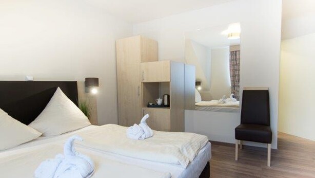 A hotel room with two beds, a wooden wardrobe, a chair, and a mirror. - Baums Rheinhotel (Boppard)