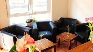 A room with two black leather sofas, a wooden coffee table, and a small table with a vase of pink flowers. - Baums Rheinhotel (Boppard)