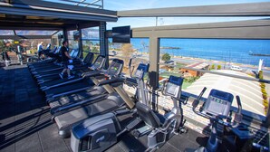 Une salle de sport équipée de plusieurs tapis de course et de vélos d’exercice, offrant une vue sur un plan d’eau et sur le paysage urbain.