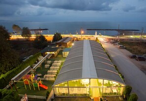 Ein großer, überdachter Außenbereich mit gewölbter Dachkonstruktion, Sitzgelegenheiten und einem Spielplatz.