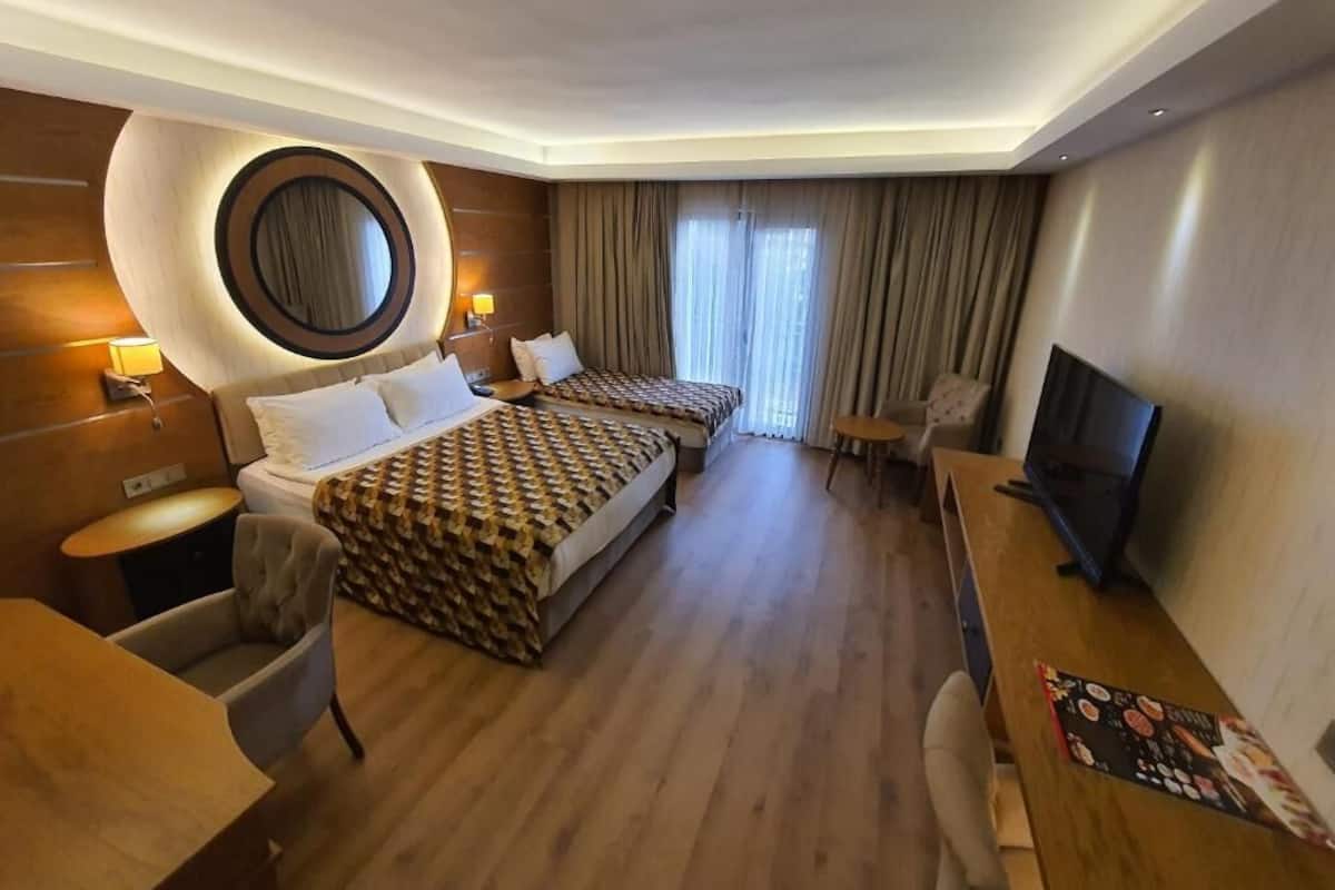 A hotel room with a large bed, a desk, a chair, a TV, and a circular mirror on the wall.