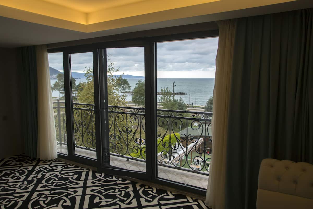 A hotel room with a large balcony, a patterned floor, and a view of the sea and mountains.