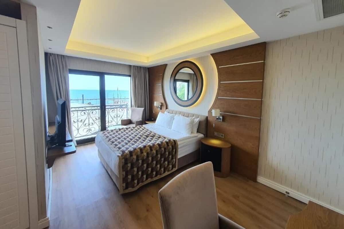 A hotel room with a bed, bedside table, and a large window with a view.
