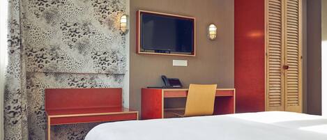 Una habitación de hotel con cama, escritorio, silla, televisor y armario.