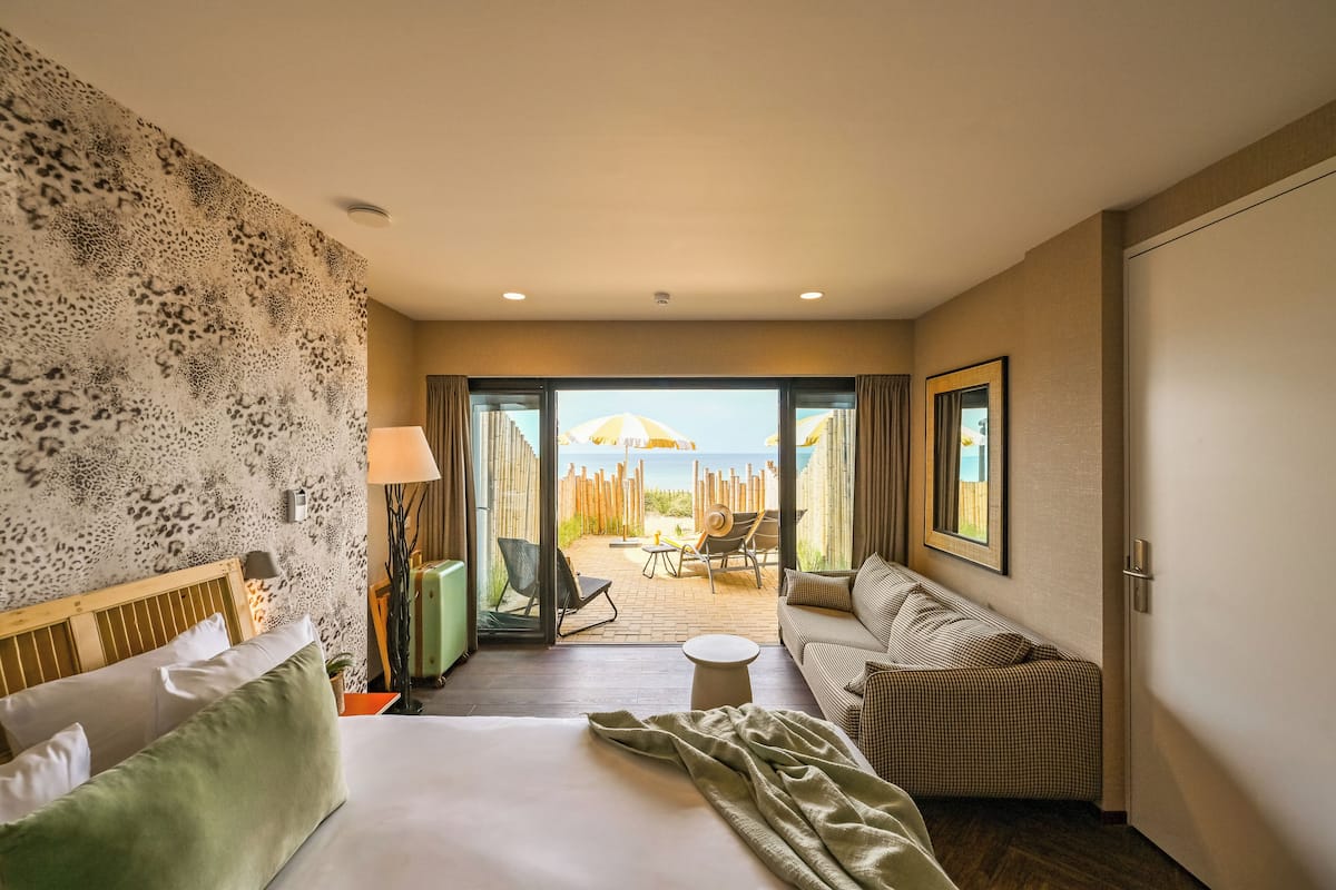 Een hotelkamer met een bed, een sofa, een tafeltje en uitzicht op het strand door een glazen deur.