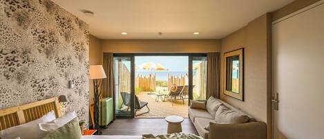 Une chambre d’hôtel avec un lit, un canapé, une petite table et une vue sur la plage, visible à travers une porte vitrée.