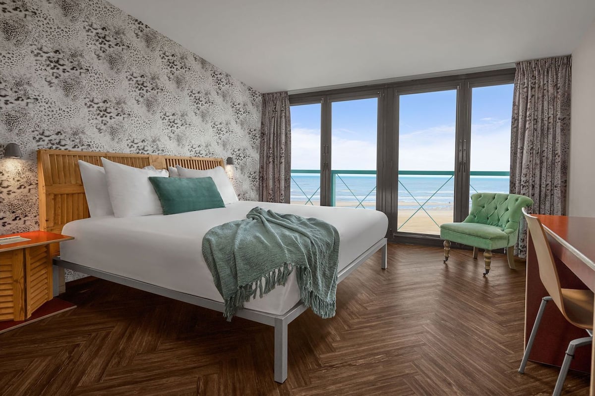 Een hotelkamer met een bed, een bureau, een stoel en uitzicht op het strand.