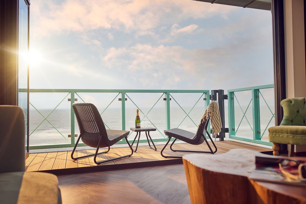 Een balkon met rieten stoelen, een kleine tafel met een fles en uitzicht op de oceaan.