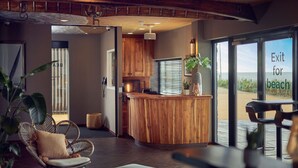 A modern interior with a wooden reception desk, a seating area with wicker chairs, and a view of the beach through large windows. - Beachhouse Hotel (Zandvoort)