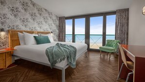 A hotel room with a bed, a desk, and a view of the beach. - Beachhouse Hotel (Zandvoort)