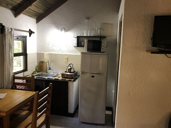 Cocina compacta con refrigerador, microondas, hervidor y pileta.