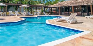 A swimming pool with lounge chairs and umbrellas, surrounded by a covered area with tables and chairs. - Rede Andrade Estrela Dalva Centro (Porto Seguro)