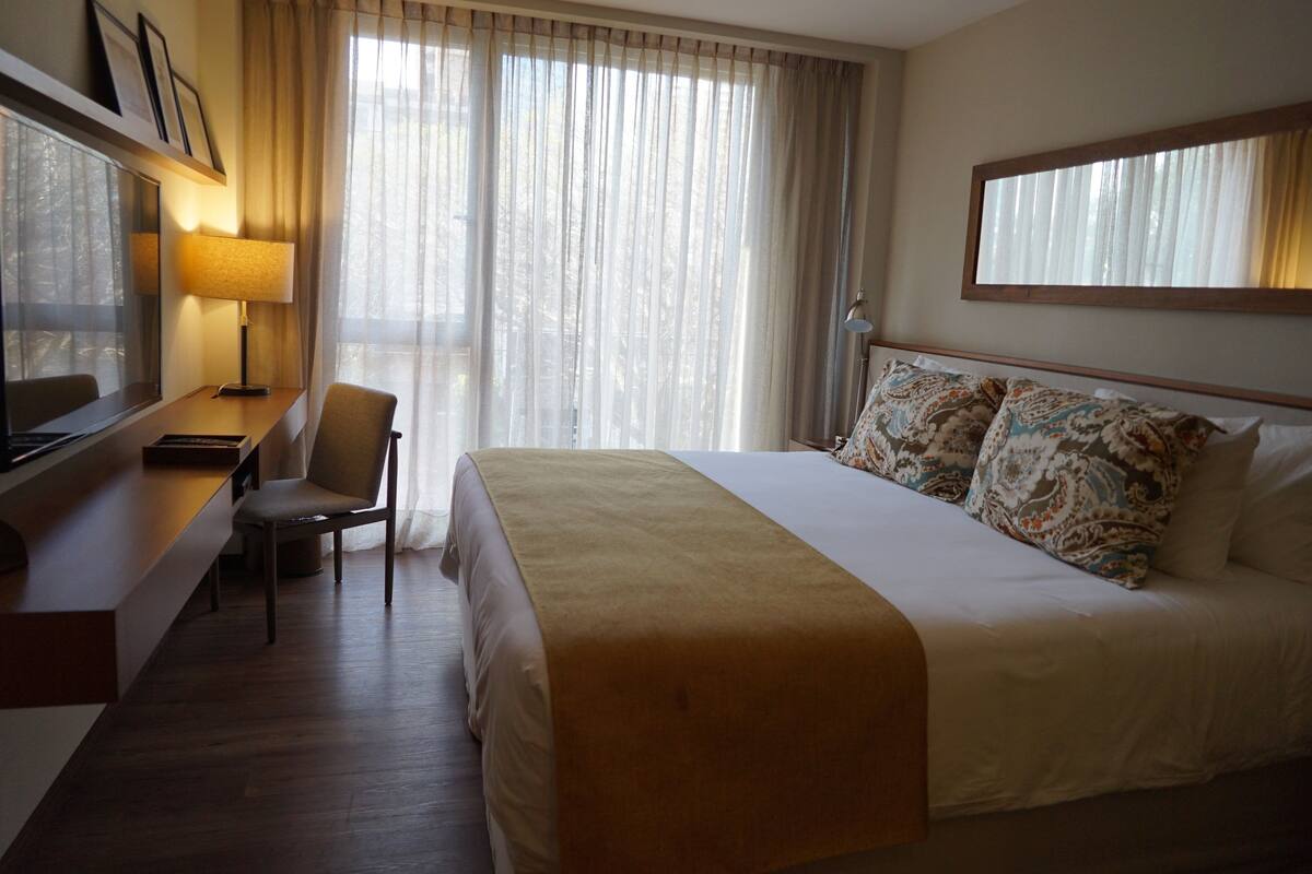 Een hotelkamer met een bed, een bureau, een stoel, een televisie en een raam met gordijnen.