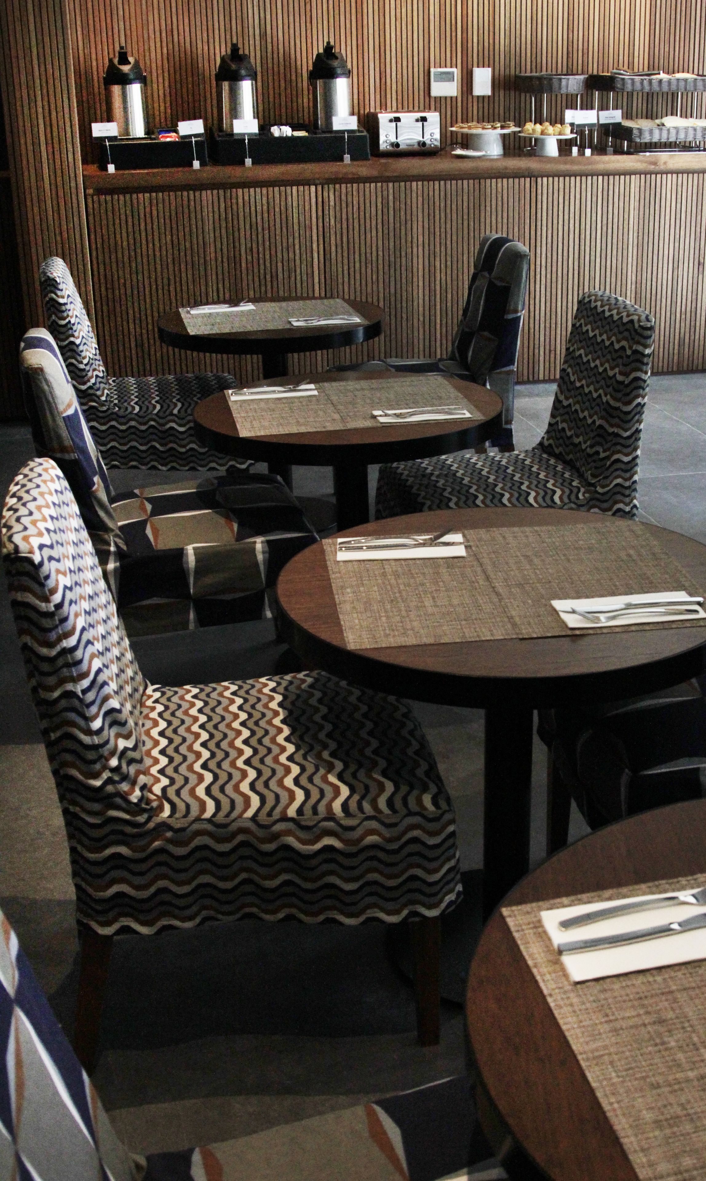 Un restaurant avec des tables rondes et des chaises à motifs, un comptoir avec des machines à café et un mur en bois.