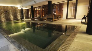 Une piscine intérieure avec des chaises longues et un mur en pierre.