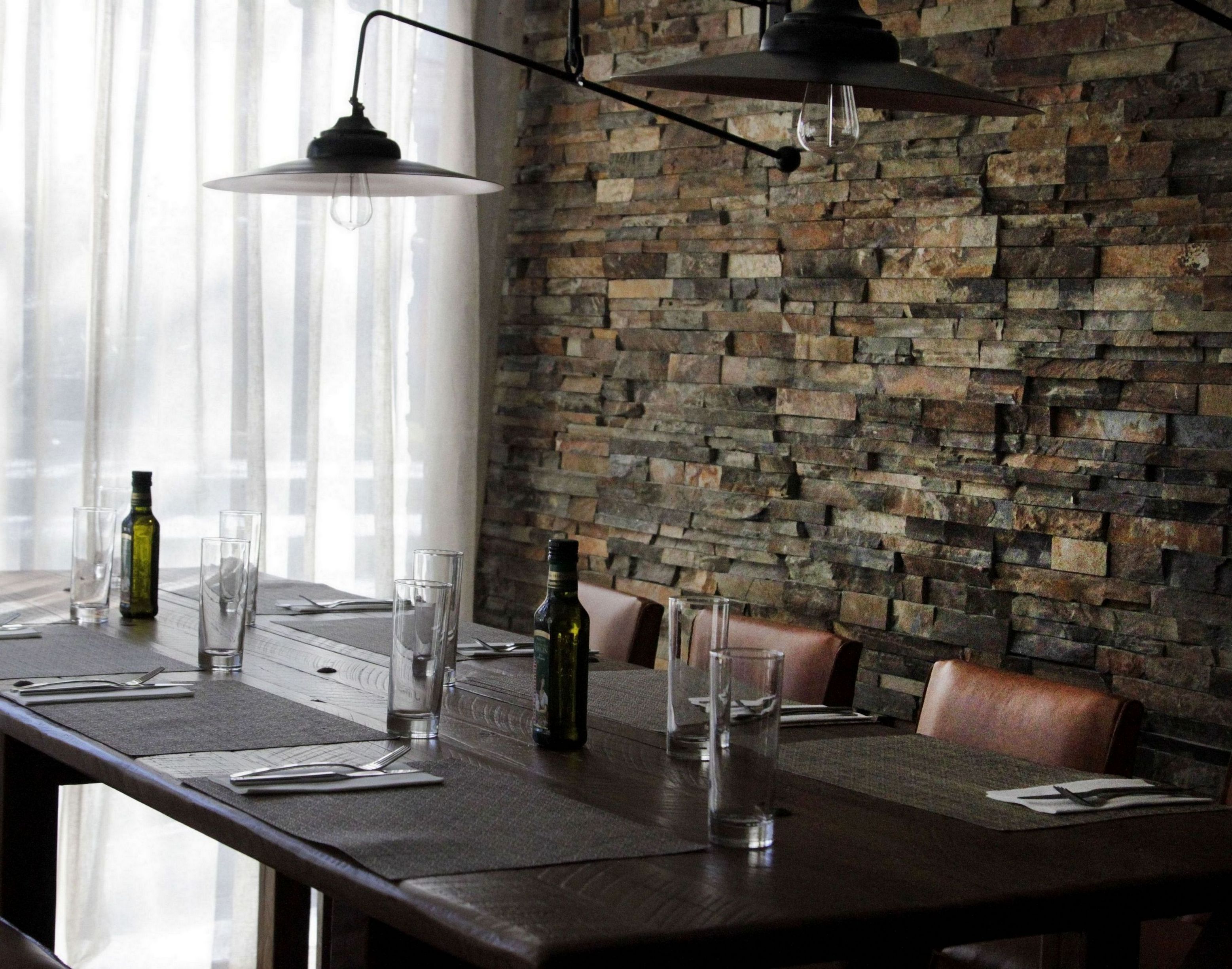 Un restaurante con pared de piedra, mesas de madera y lámparas colgantes.