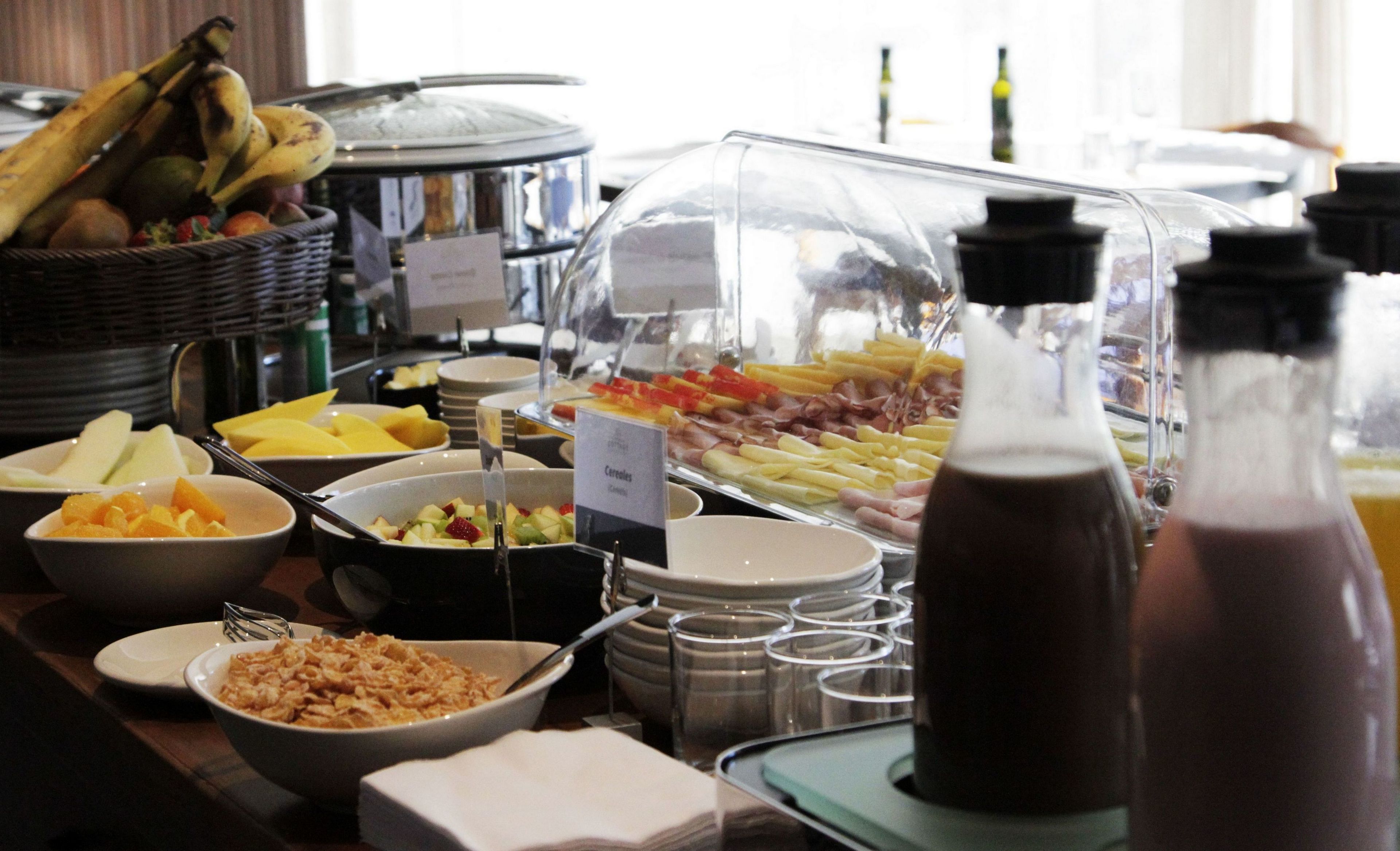 A buffet with various food items including fruits, cereals, and a beverage dispenser.