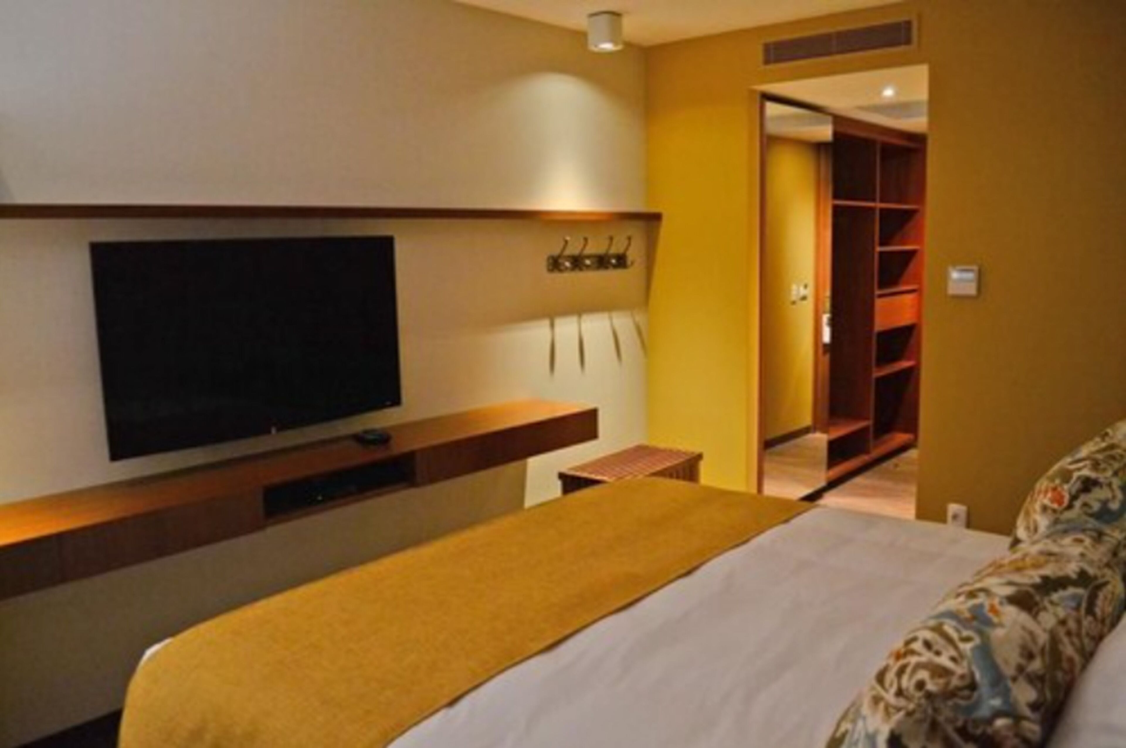 Una habitación de hotel con cama, televisor montado en la pared, mesita de noche y armario.