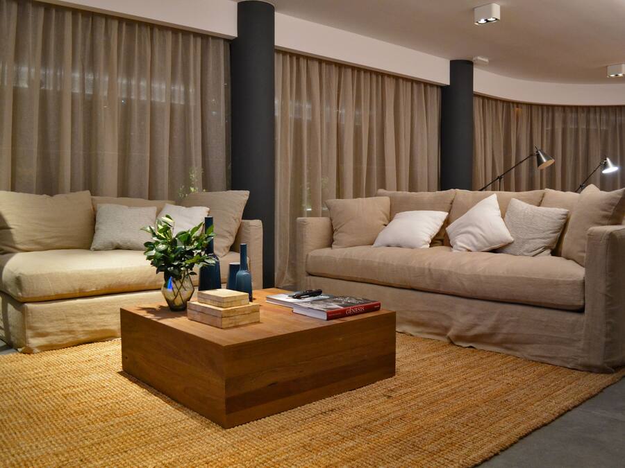 Una sala de estar moderna con dos sofás color beige, una mesa de centro de madera y un ventanal con cortinas.