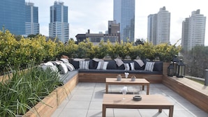 Un espace extérieur aménagé avec des canapés et des tables, entouré de plantes et offrant une vue sur le paysage urbain.