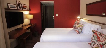 Habitación de hotel con dos camas, televisor, escritorio y espejo.