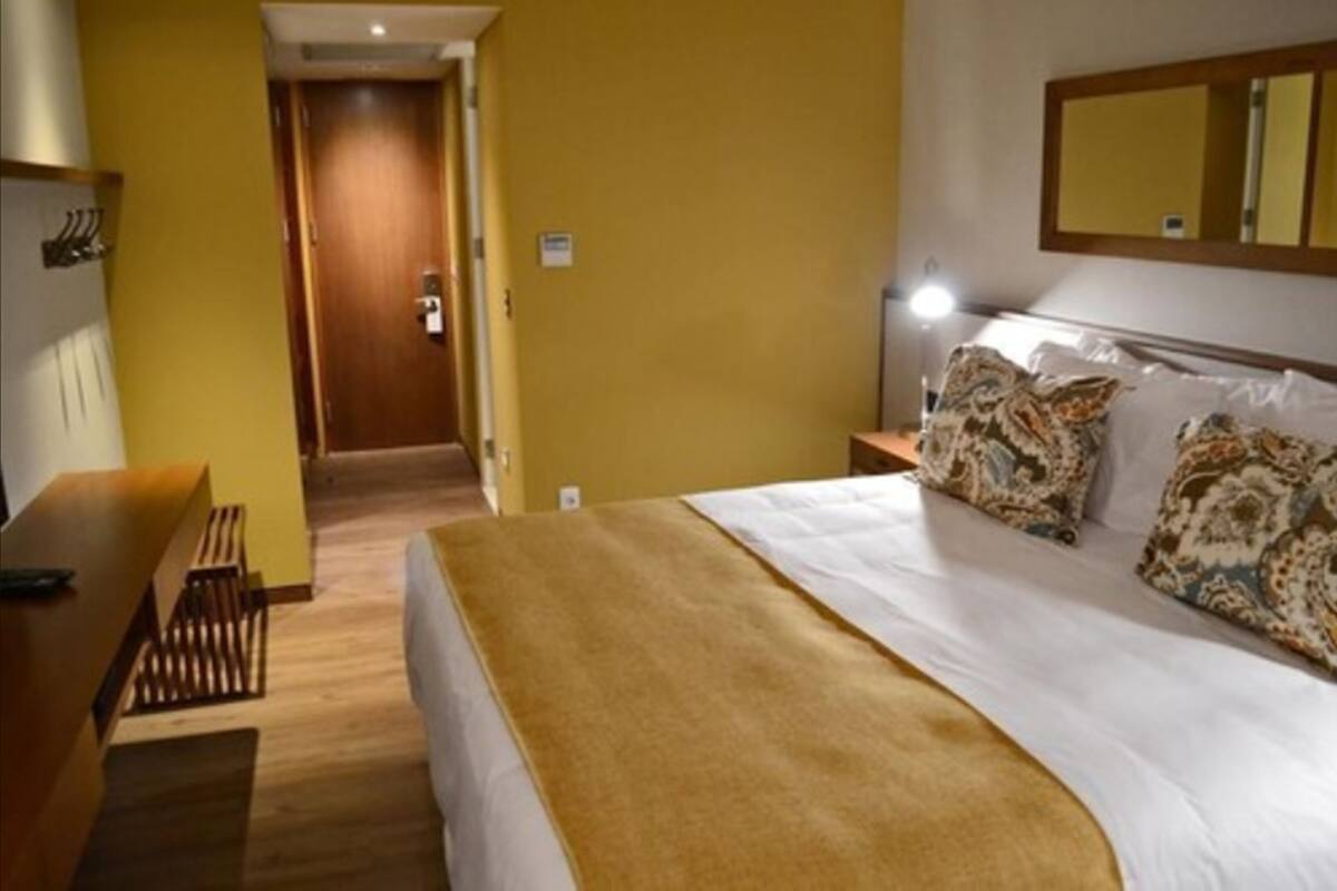 Een hotelkamer met een bed, nachtkastje, lamp en een spiegel aan de muur.