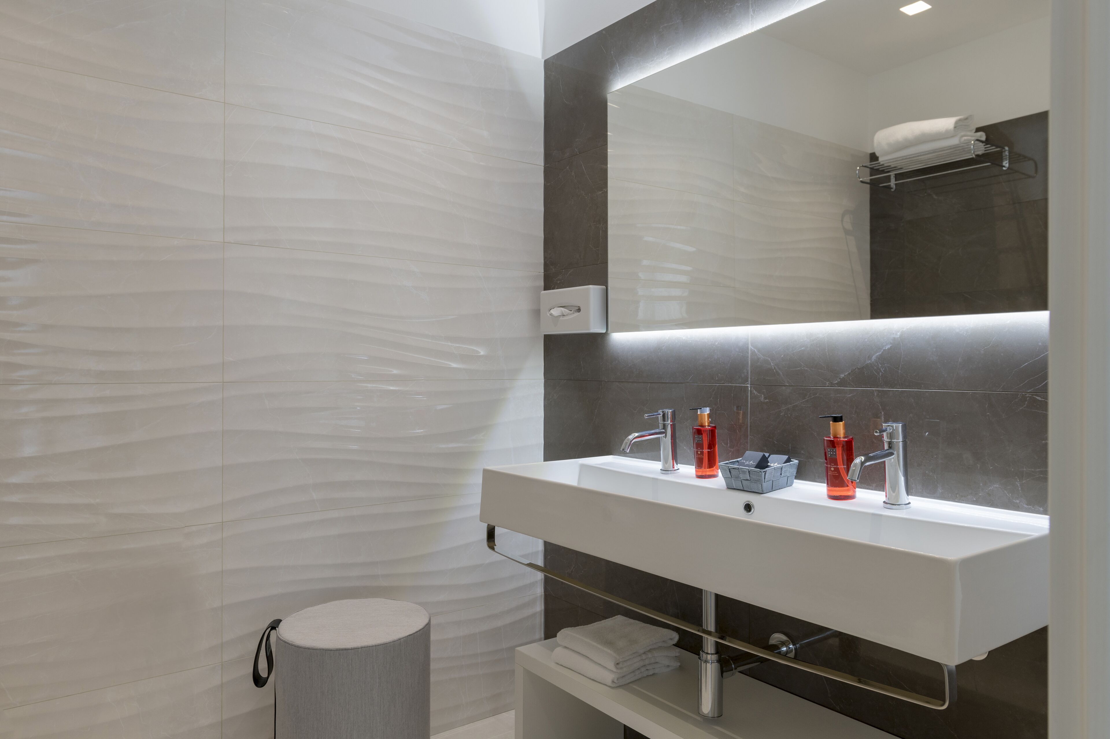 A modern bathroom with a white vanity, a large mirror, and a towel rack.