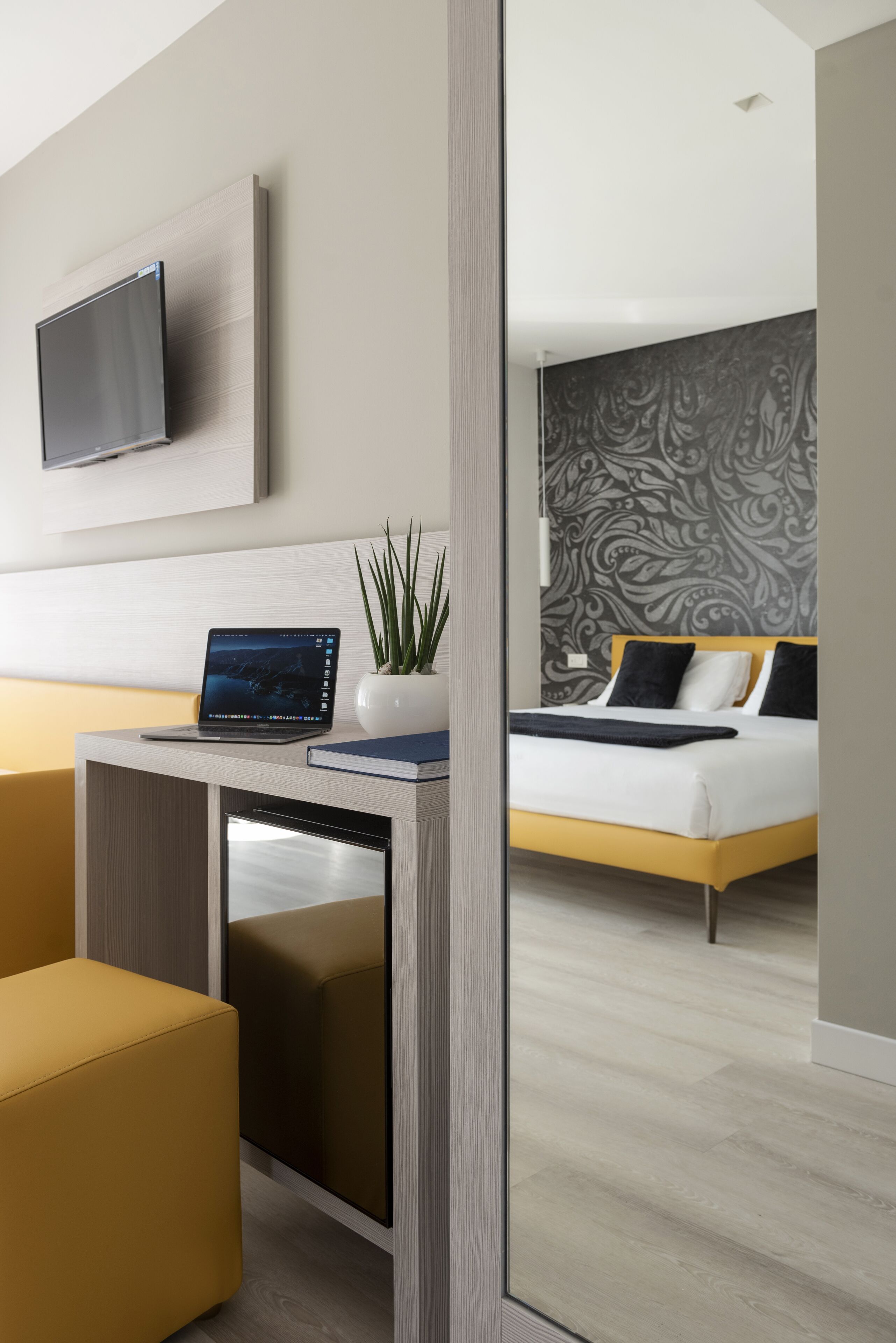 Habitación de hotel moderna con cama, escritorio, laptop, televisor y planta en maceta.