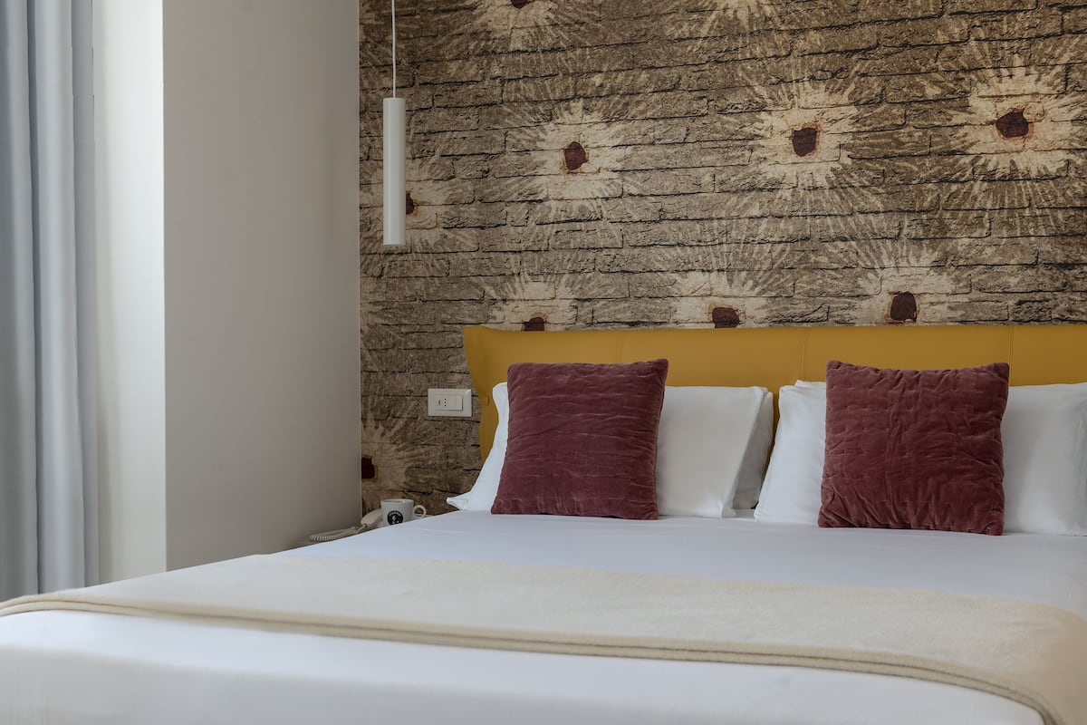 Una cama con almohadas blancas y burdeos, un cabecero de madera y una pared con diseño de ladrillo.