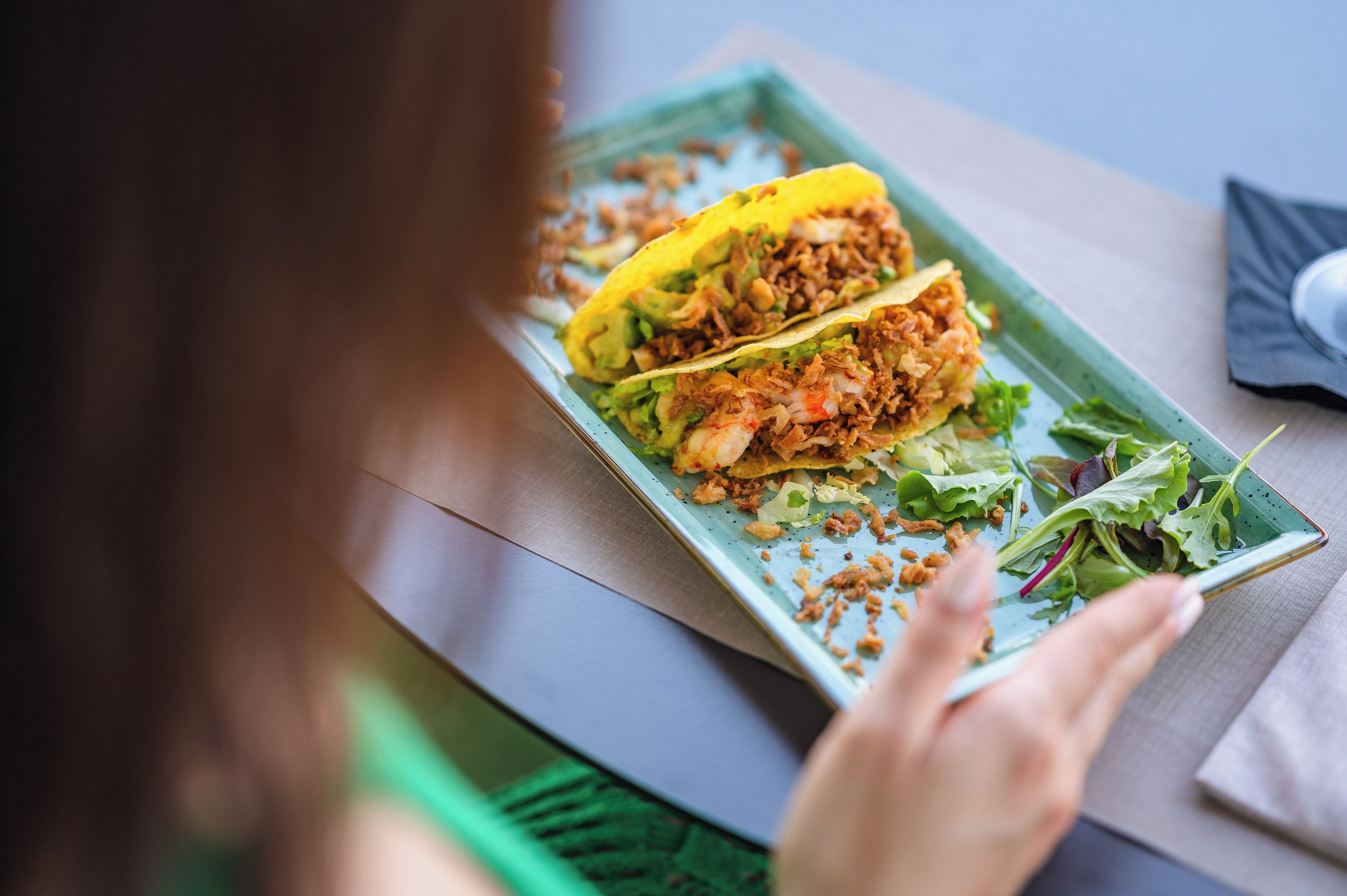 Une assiette de tacos, accompagnée d’une assiette verte et d’une serviette, est posée sur une table.
