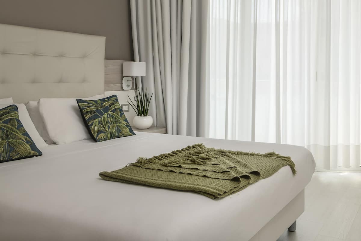 Un dormitorio moderno con una cama grande, ropa de cama blanca y una manta verde.