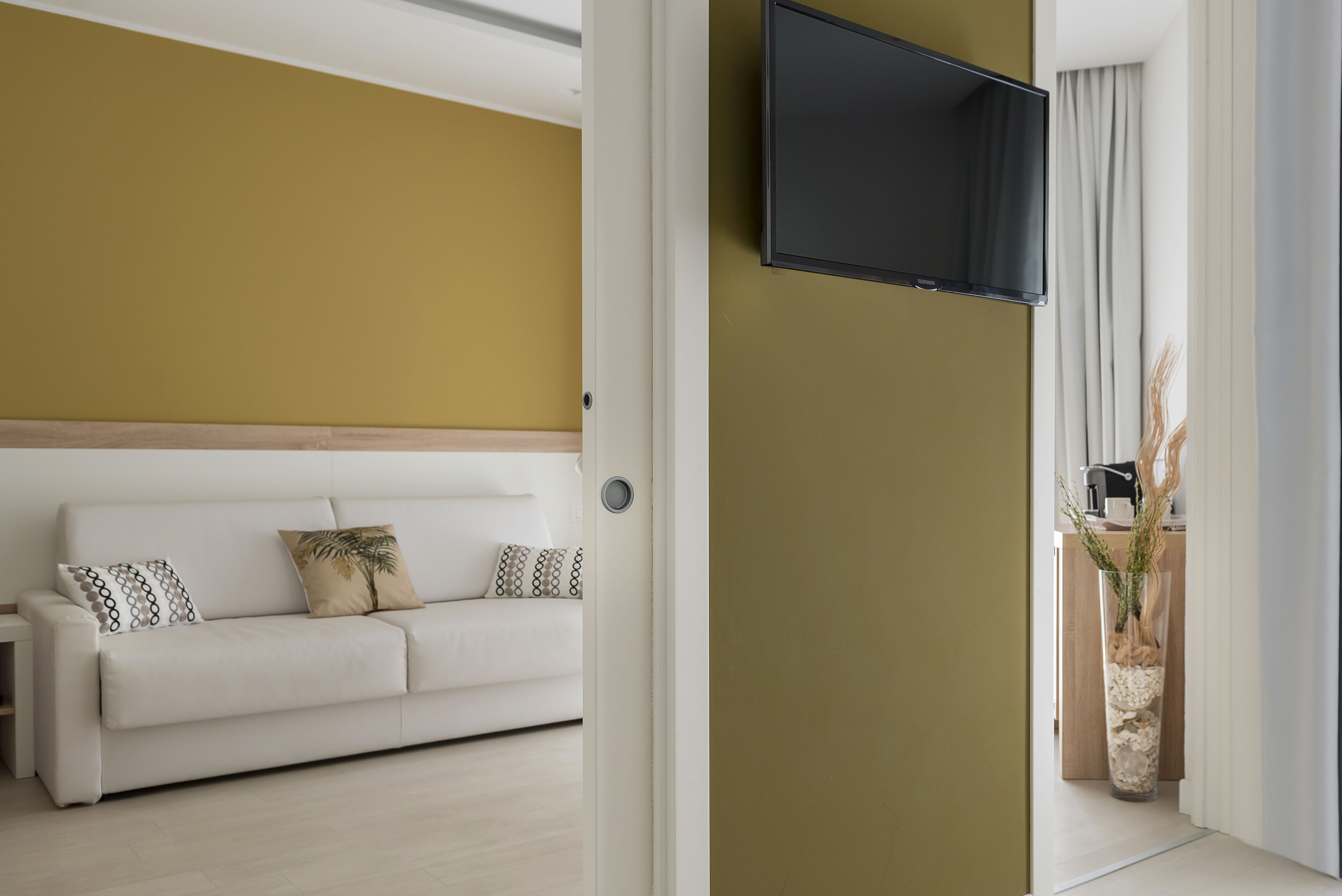 Ein modernes Wohnzimmer mit einem weißen Sofa, einem flachbildfernseher an der Wand und einem großen Fenster mit Vorhängen.