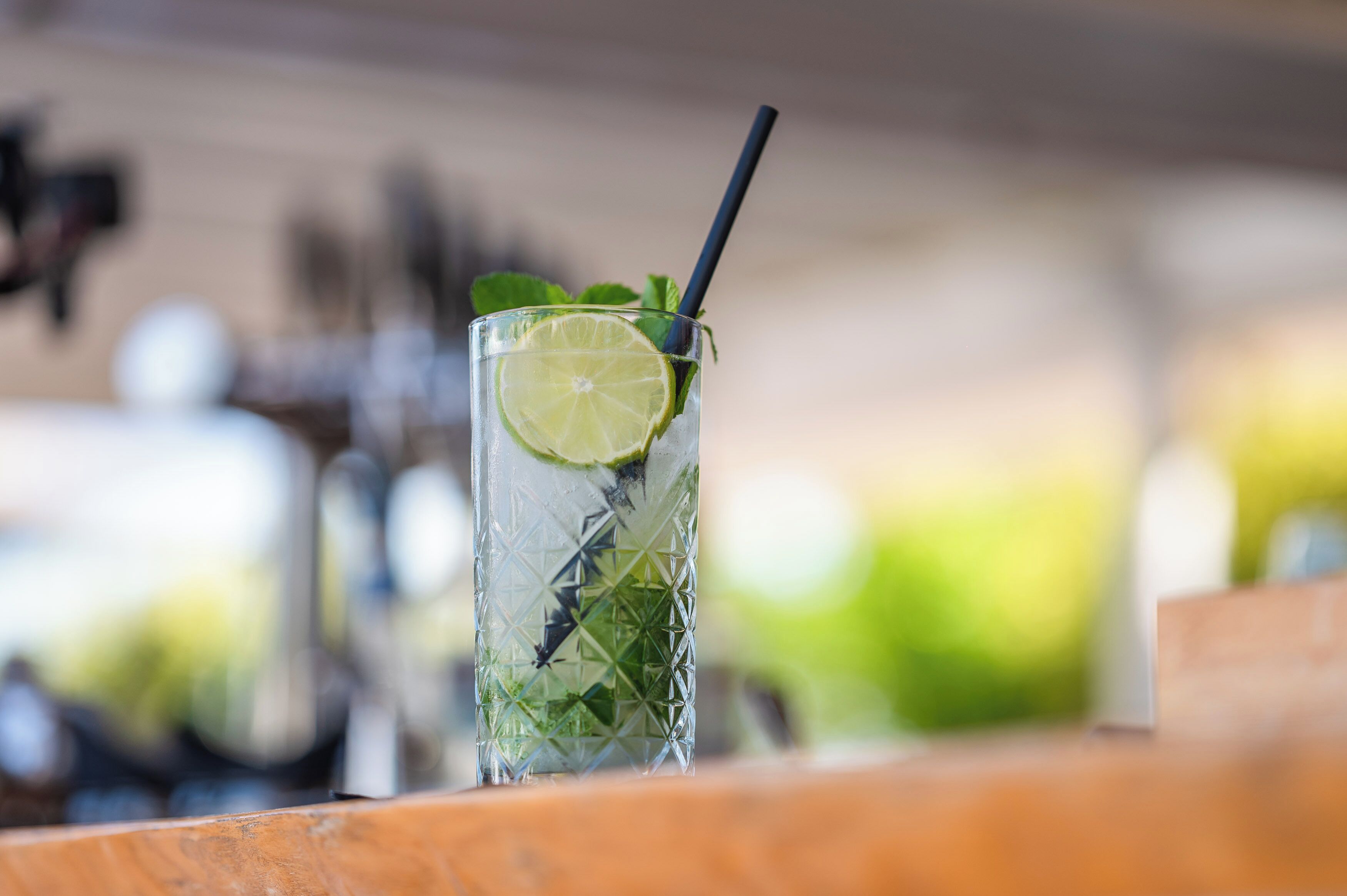 A clear glass with a lime slice and mint leaves, a black straw, and a textured pattern on the glass.
