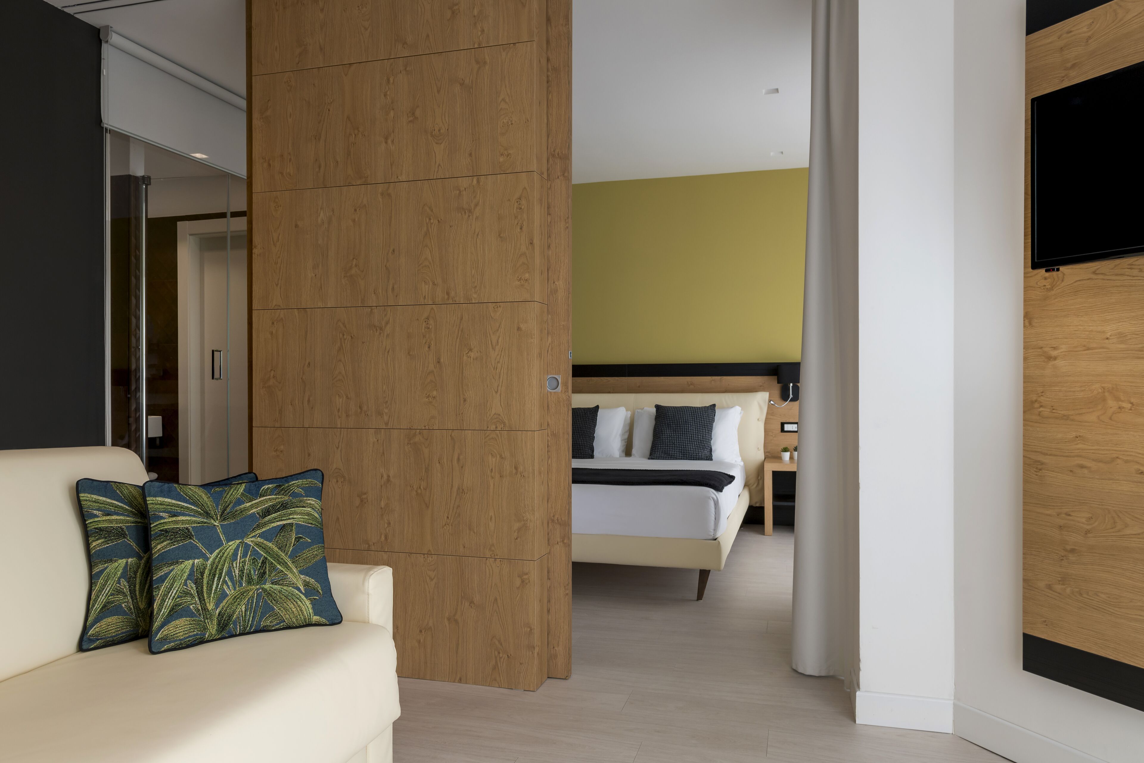 Una habitación de hotel moderna con una pared de acento de madera, una cama con ropa blanca y un televisor montado en la pared.