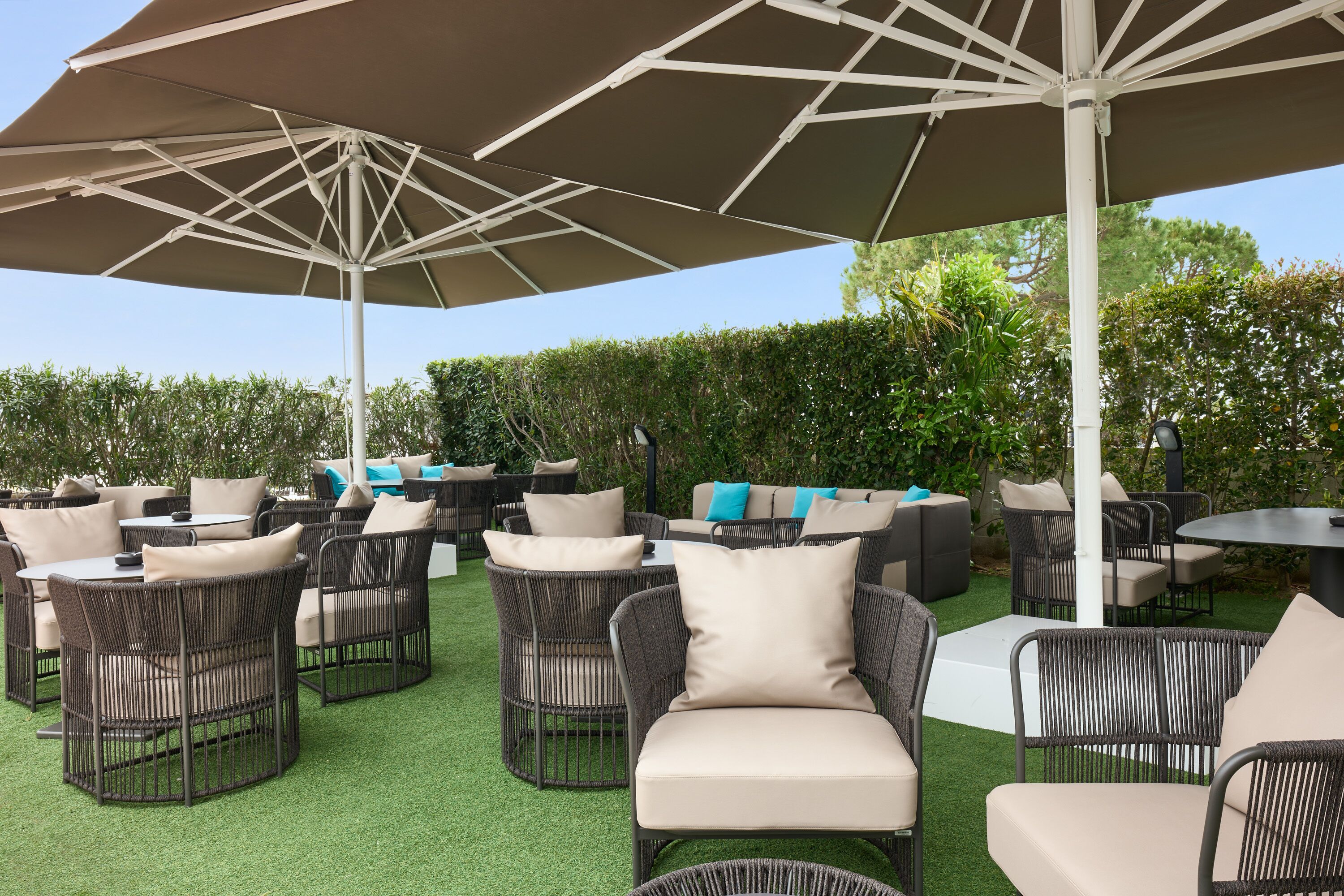 Un patio al aire libre con mobiliario de mimbre, cojines color beige y grandes sombrillas.